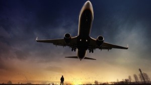 Passenger jet taking off at dusk with a silhouetted man watching it leave