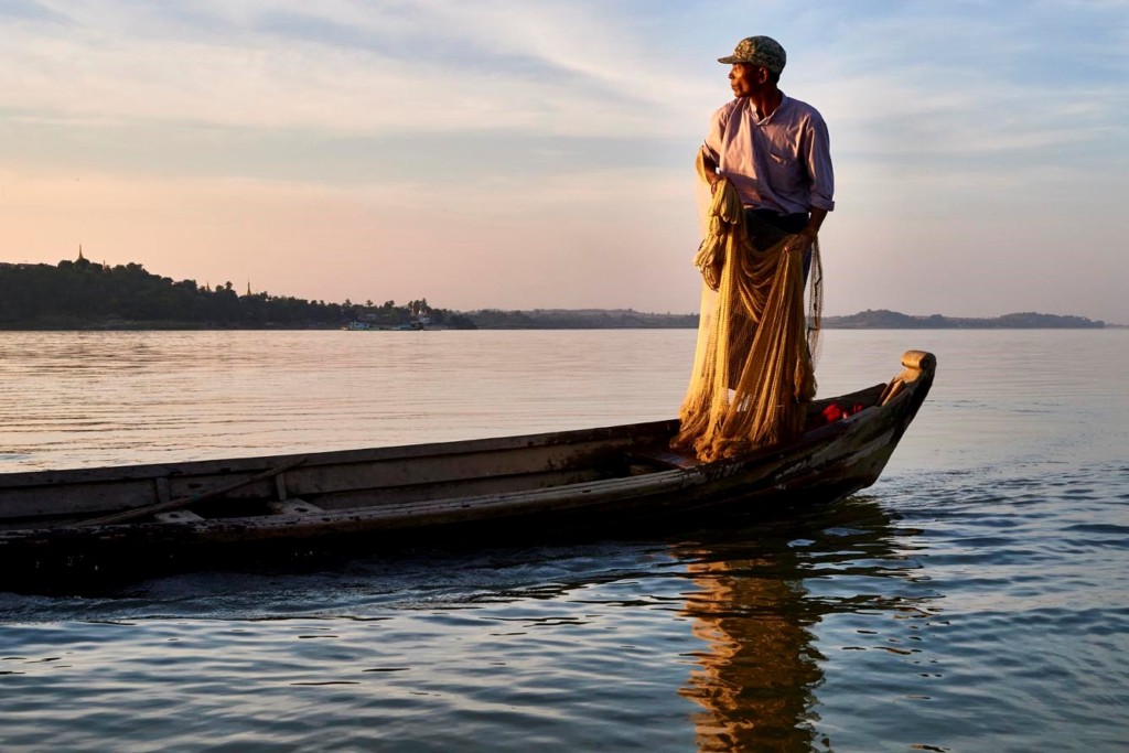 Fisherman standing in canoe holding net, waiting for the right time to cast it. Burma, Myanmar, Mandalay Division, Irrawaddy, Ayeyarwady river, fishing with dolphins.